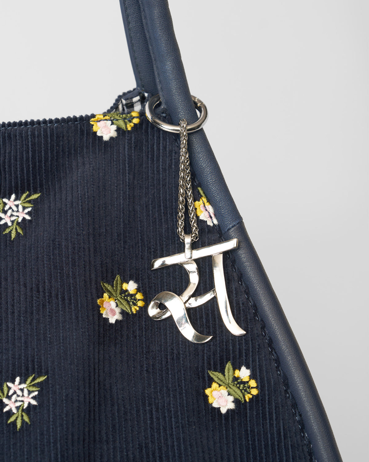 Alphabet S Bag Charm in silver hanging from a navy bag with floral embroidery.