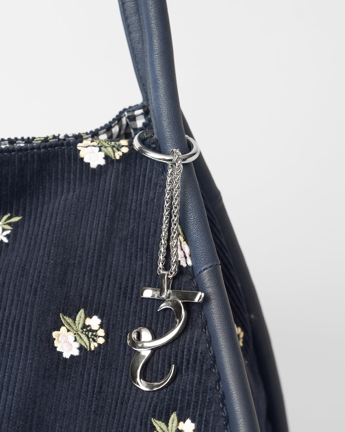 Alphabet R Bag Charm in silver hanging from a navy bag with floral embroidery.