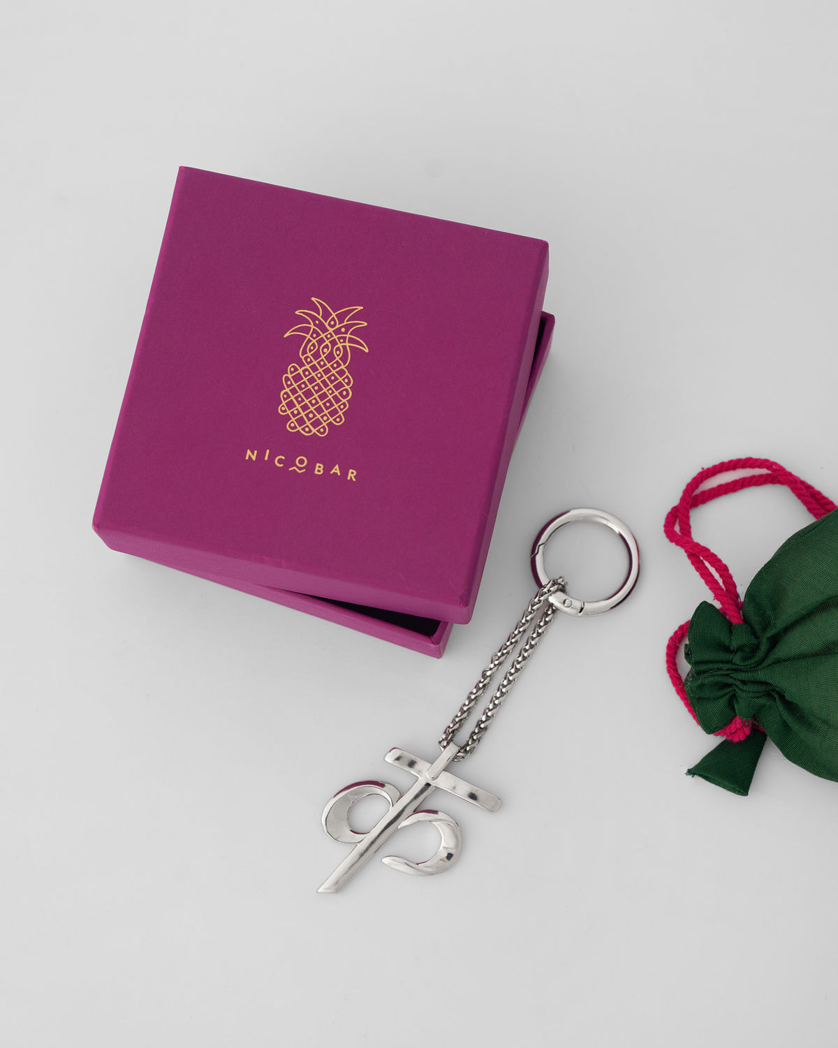 Alphabet K Bag Charm in silver beside a magenta Nicobar gift box and green pouch.