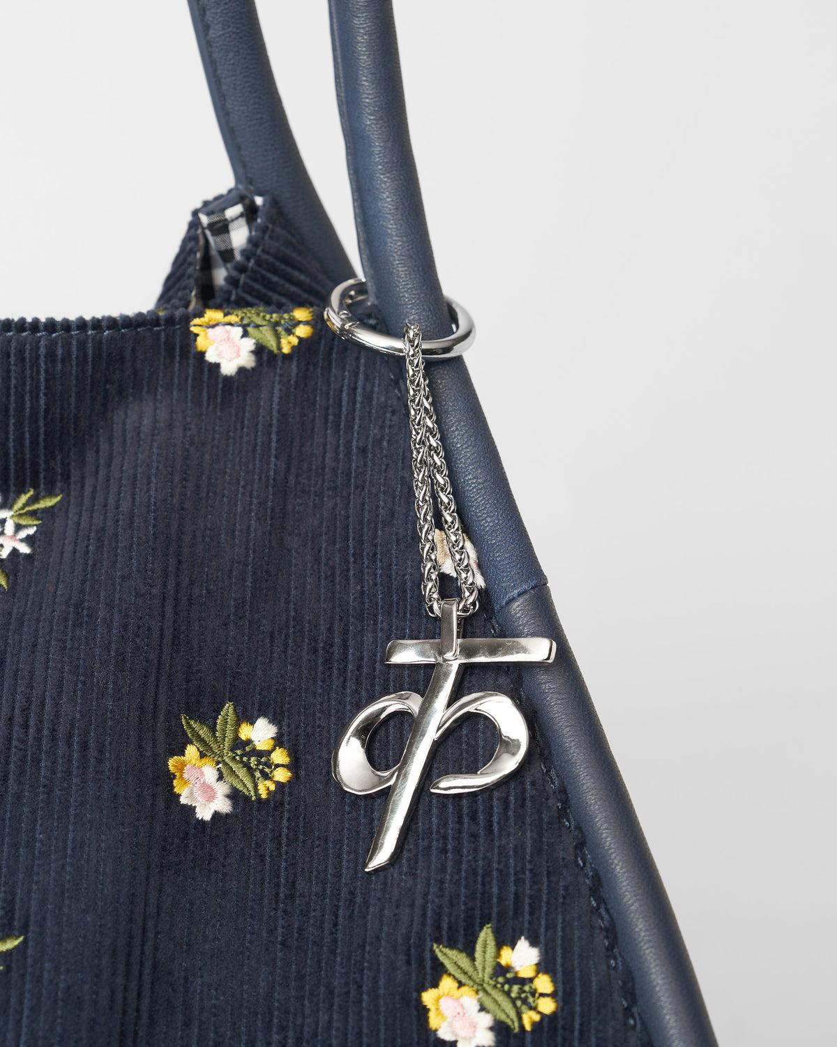 Alphabet K Bag Charm in silver hanging from a navy bag with floral embroidery.