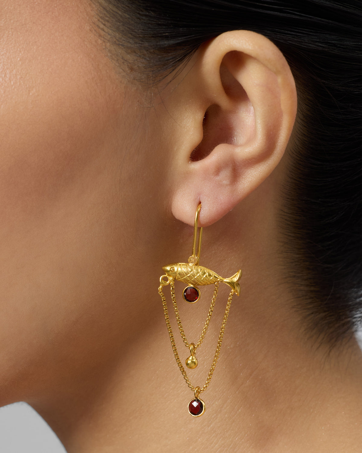 Side profile of a gold Maase fish earring with red glass drops.