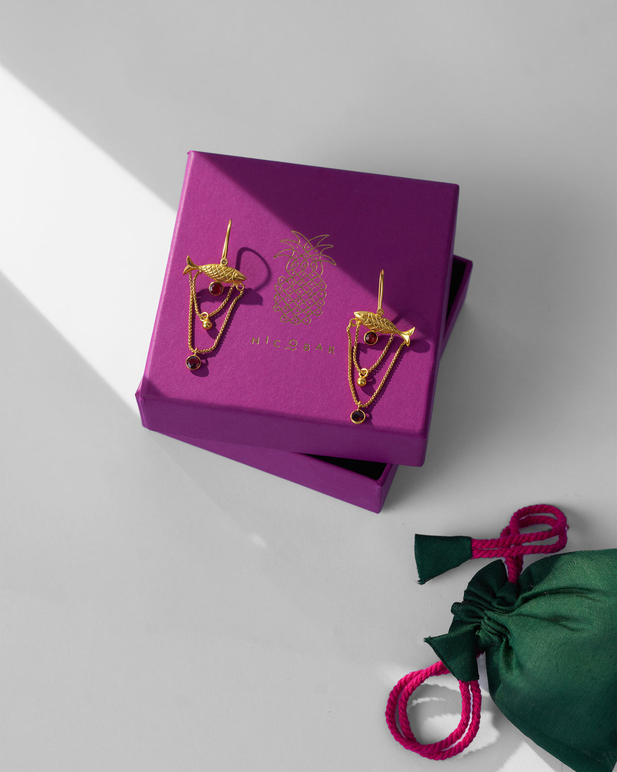 Gold Maase fish earrings on a purple Nicobar gift box.