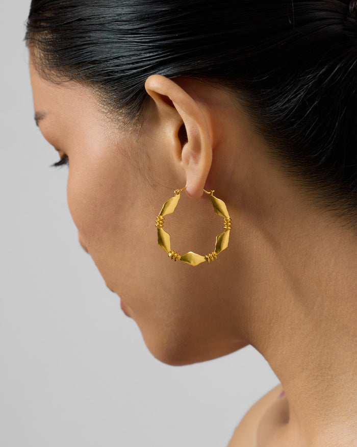 Side profile of a gold Pillar bali with geometric segments on a person.