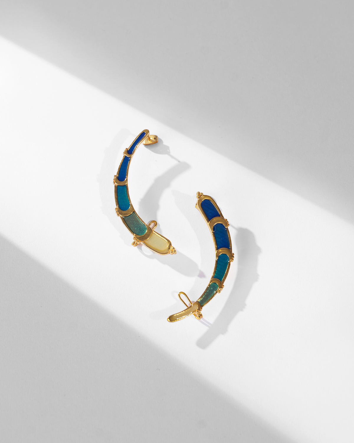 Pair of gold Rising Moon enamel crescent earrings laid flat.