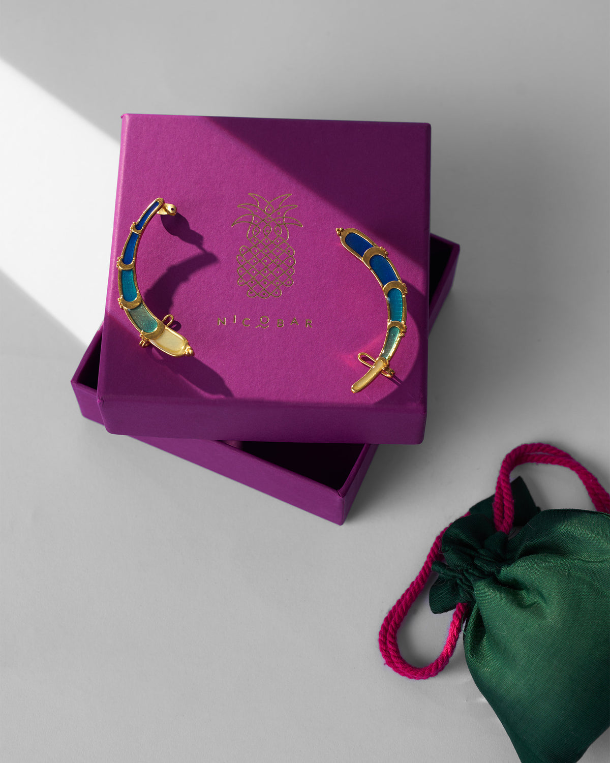 Gold Rising Moon enamel earrings on a purple Nicobar gift box.