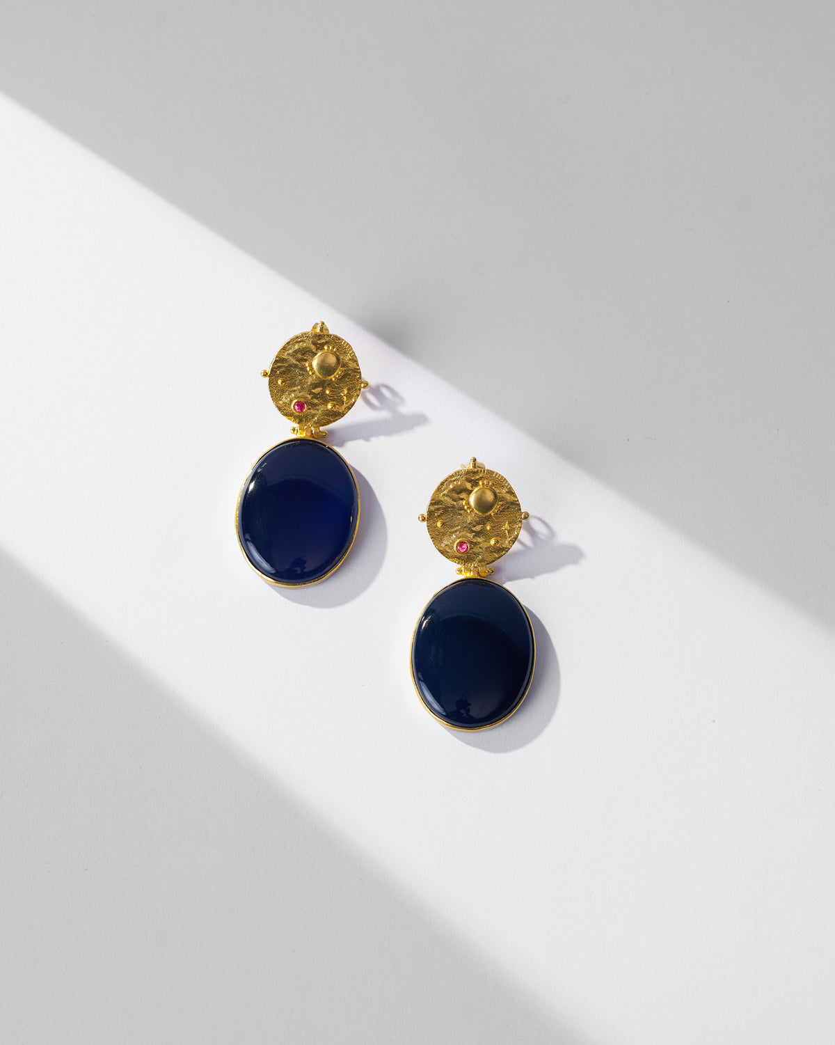 Pair of gold Nebra earrings with navy glass drops laid flat.