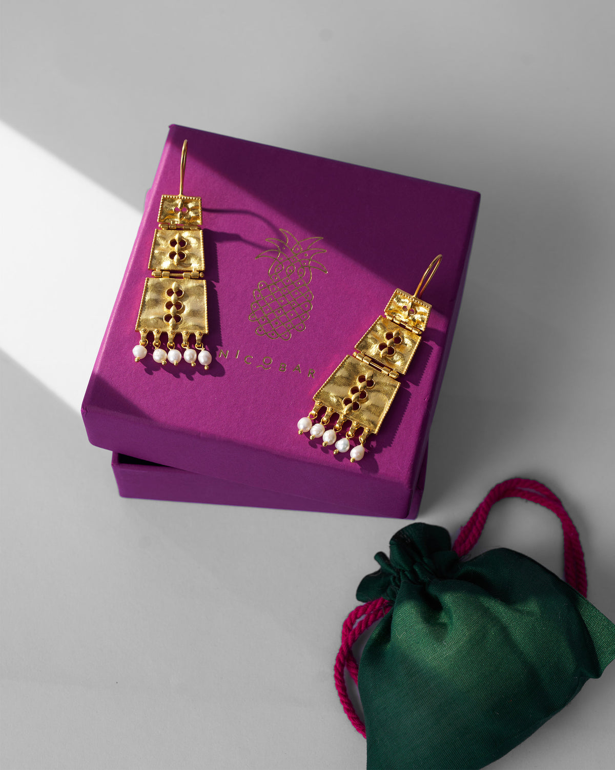 Gold column earrings on a purple Nicobar gift box.