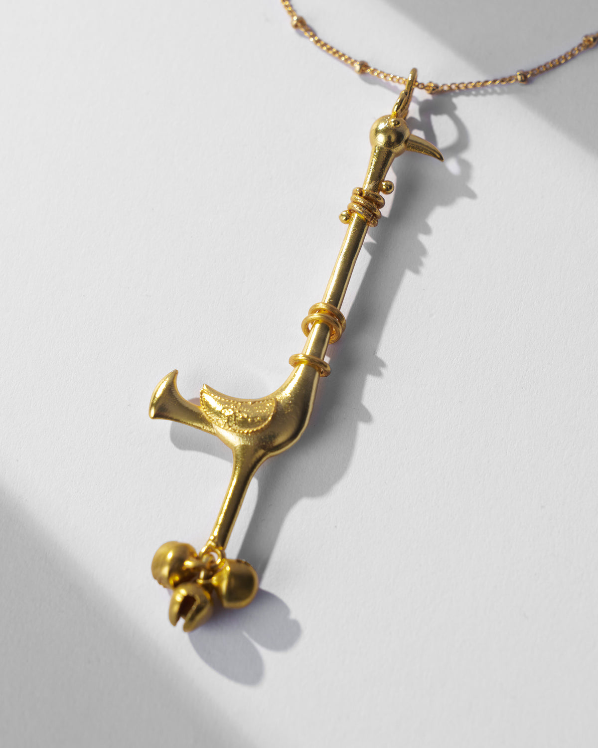Close-up of Saras necklace bird pendant with small bells at the base.