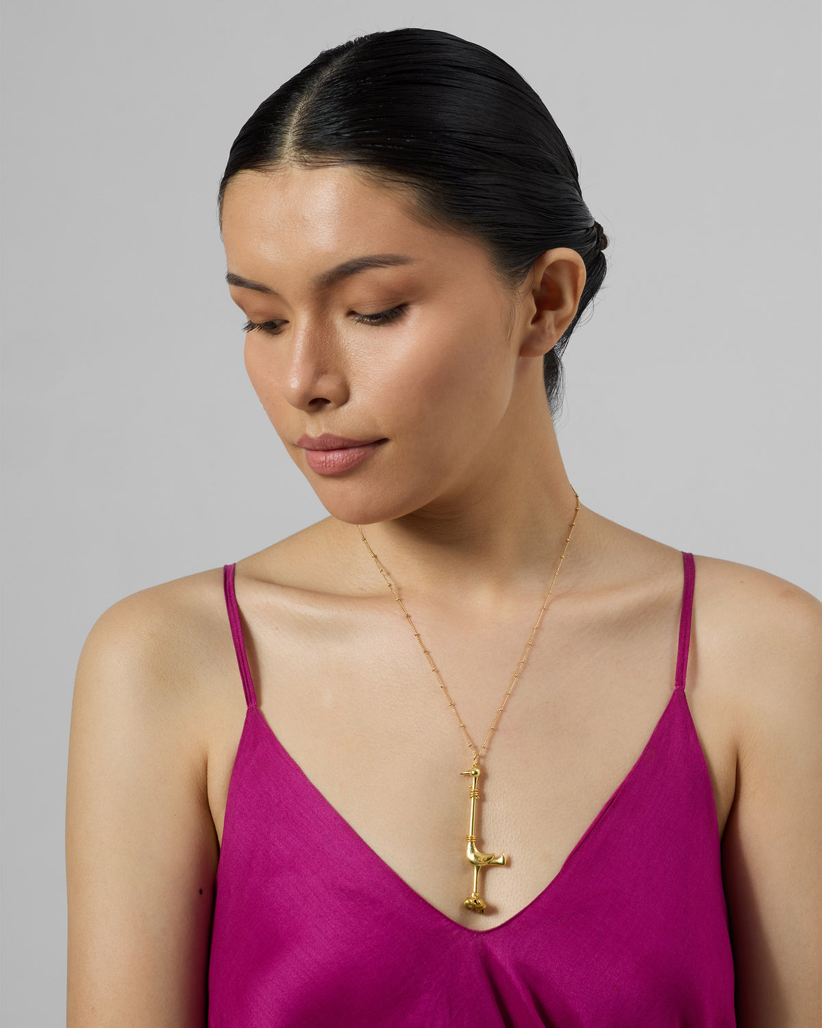 Person wearing a gold Saras necklace with a slender bird pendant.
