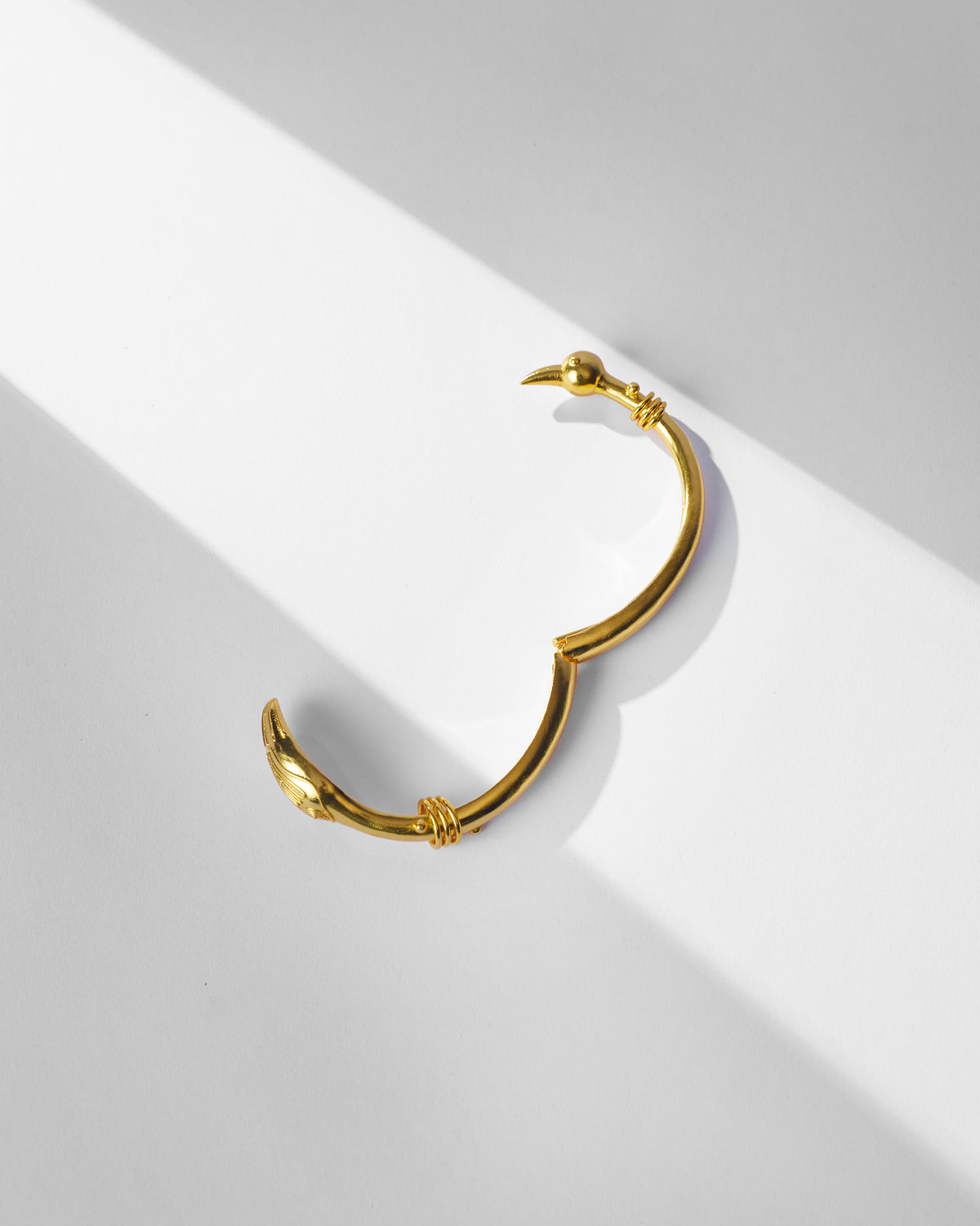 Gold Saras hinged cuff with crane-head terminals.