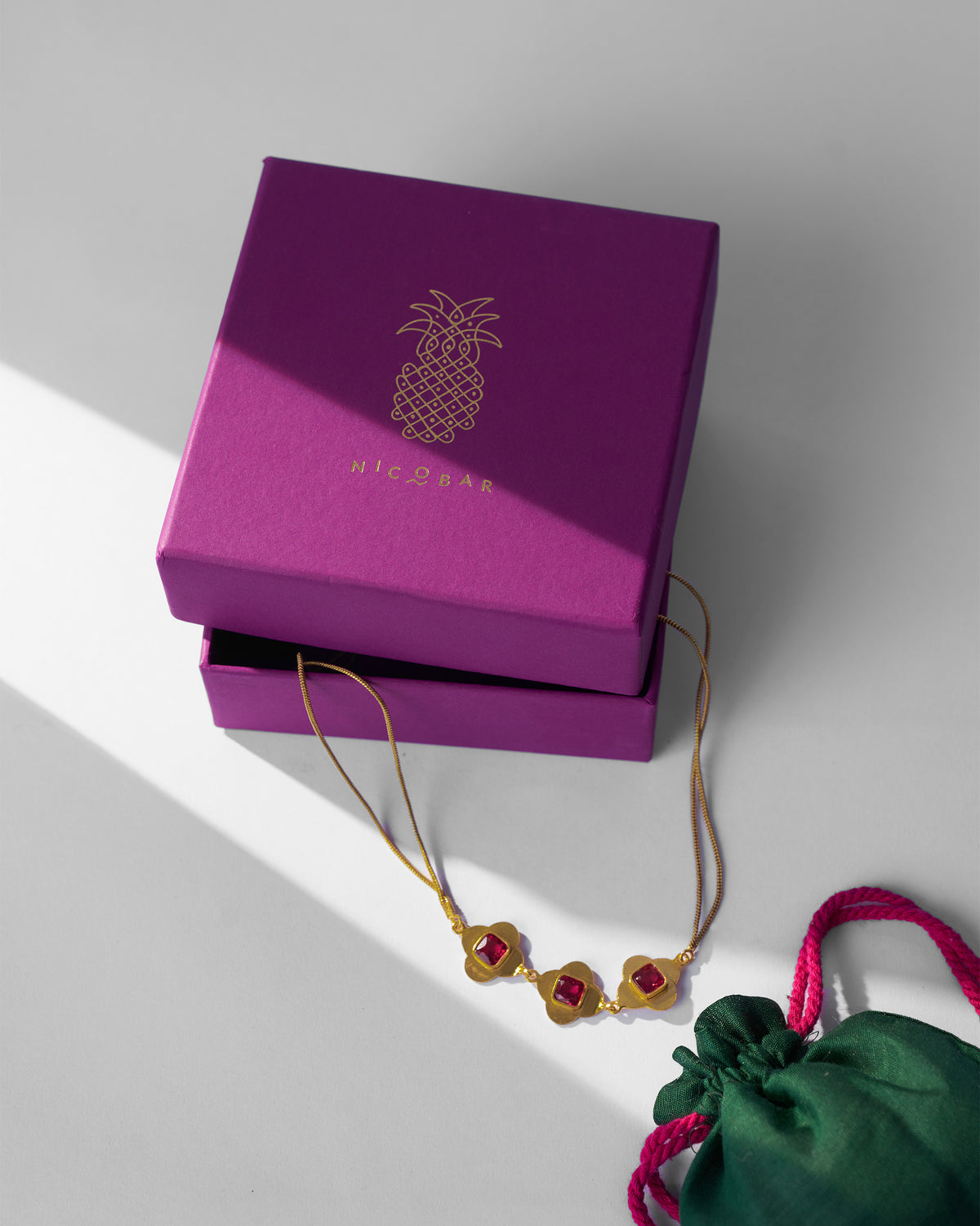 Gold Ahiliya choker with a magenta Nicobar gift box and green pouch.