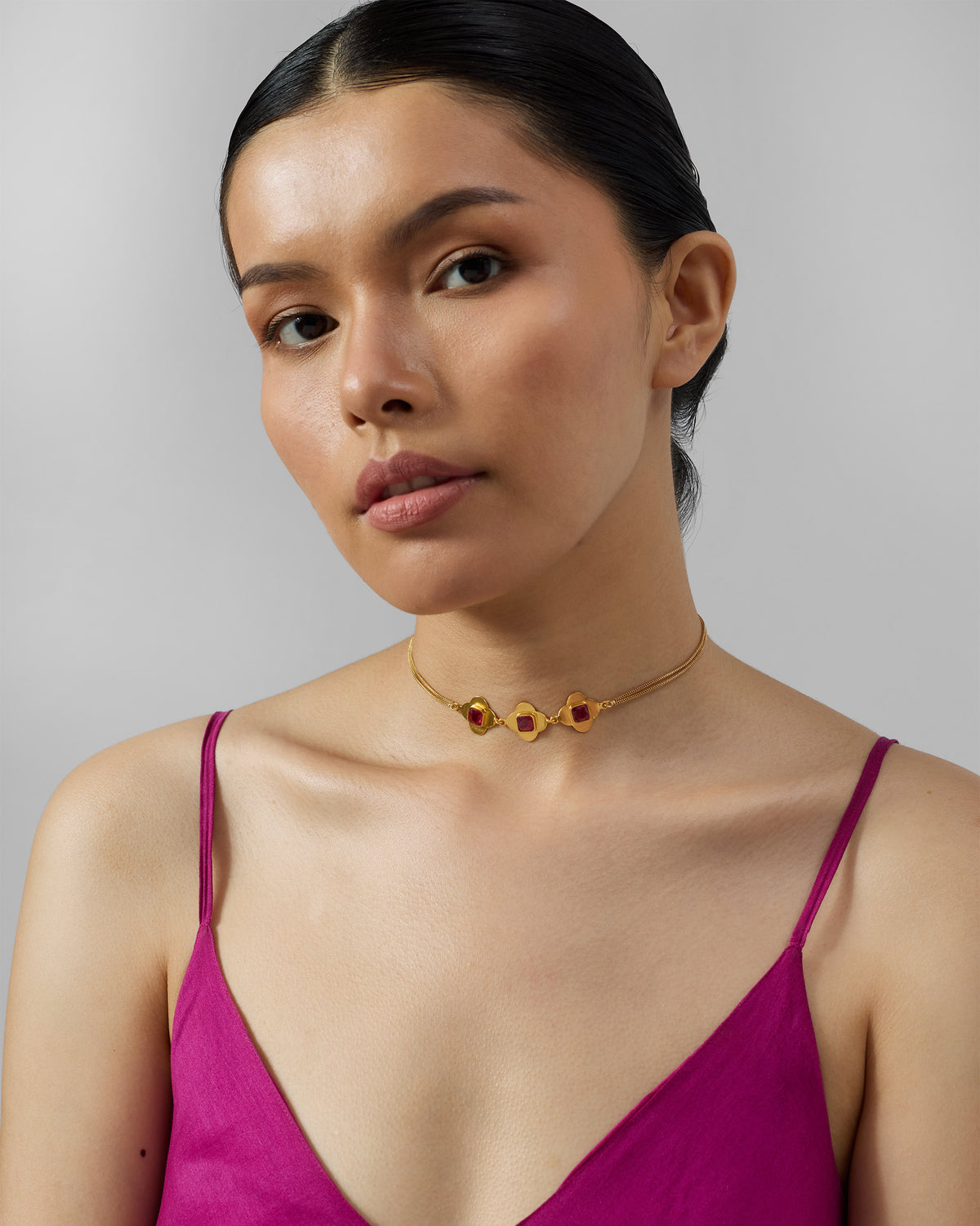 Person wearing a gold Ahiliya choker with three pink glass motifs.