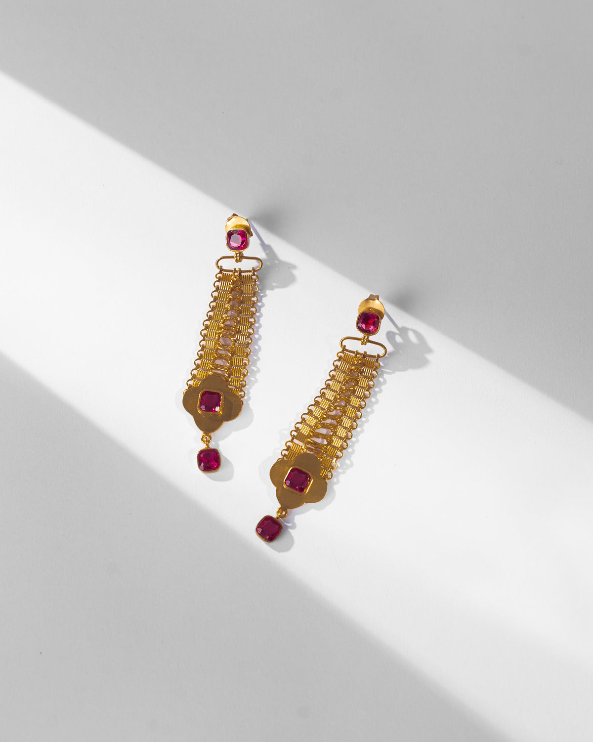 Pair of gold Ahiliya danglers with pink glass and quatrefoil drops laid flat.