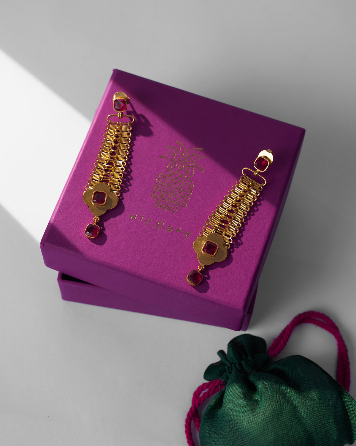 Gold Ahiliya danglers with red glass on a purple Nicobar gift box.