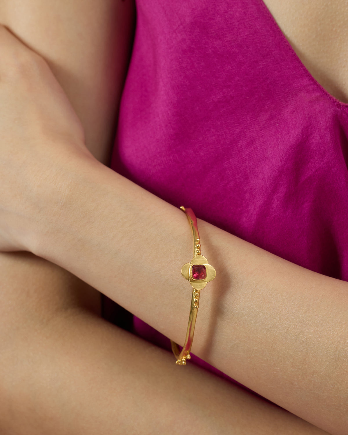 Gold Ahiliya bangle with a pink glass flower motif worn on a wrist.