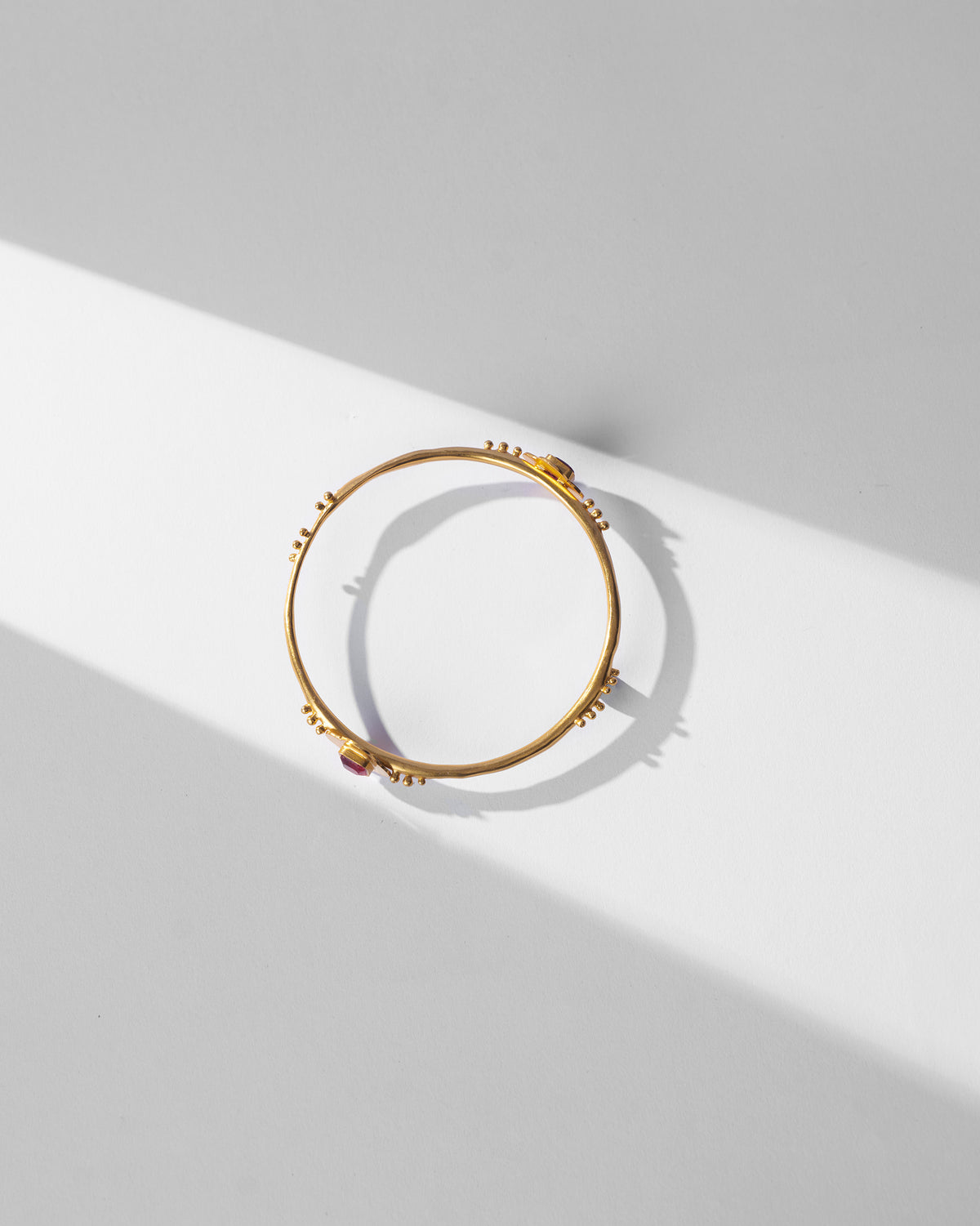 Overhead view of a gold Ahiliya bangle with pink glass accents.