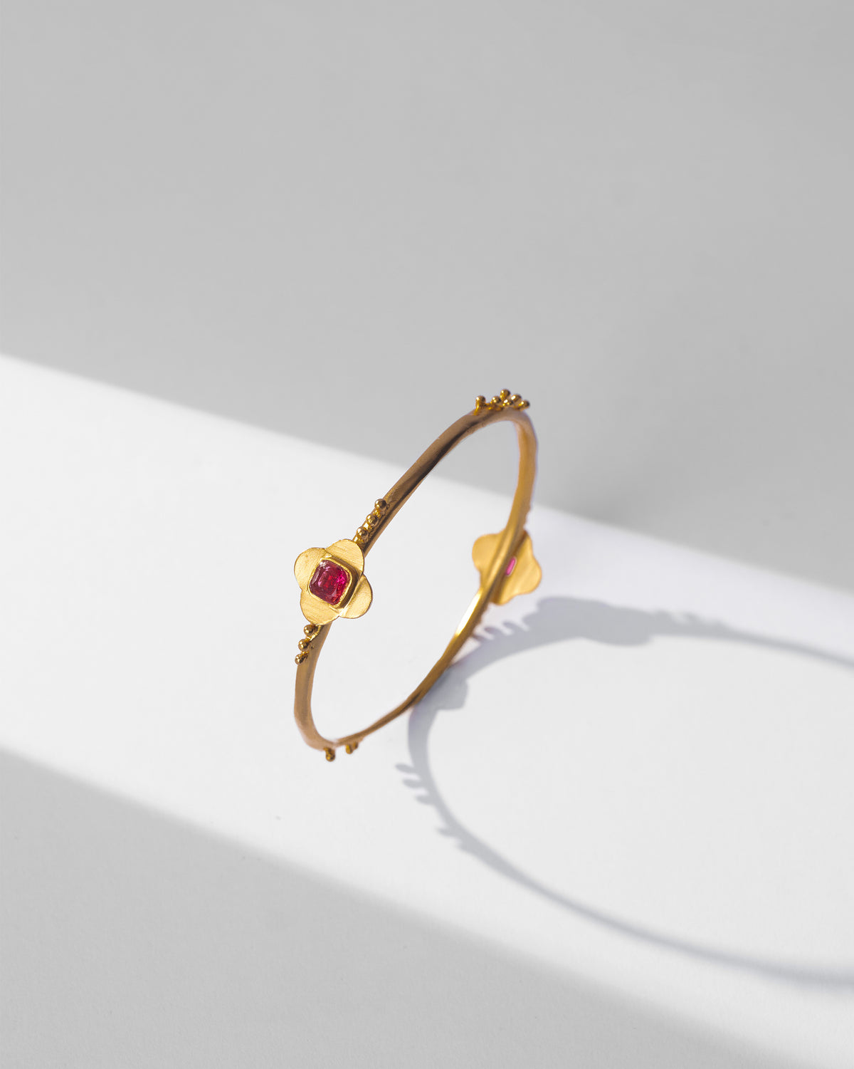 Gold Ahiliya bangle with opposing pink glass flower motifs.