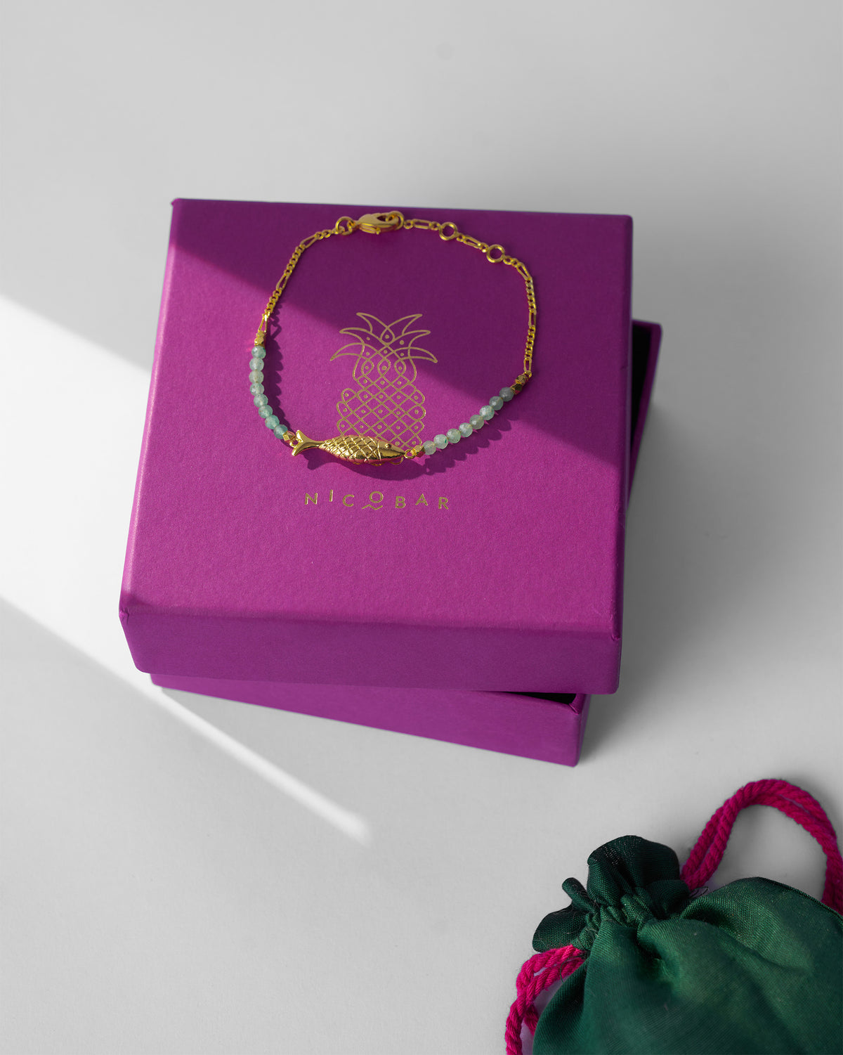 Gold Ahiliya bangle on a magenta Nicobar gift box with green pouch.
