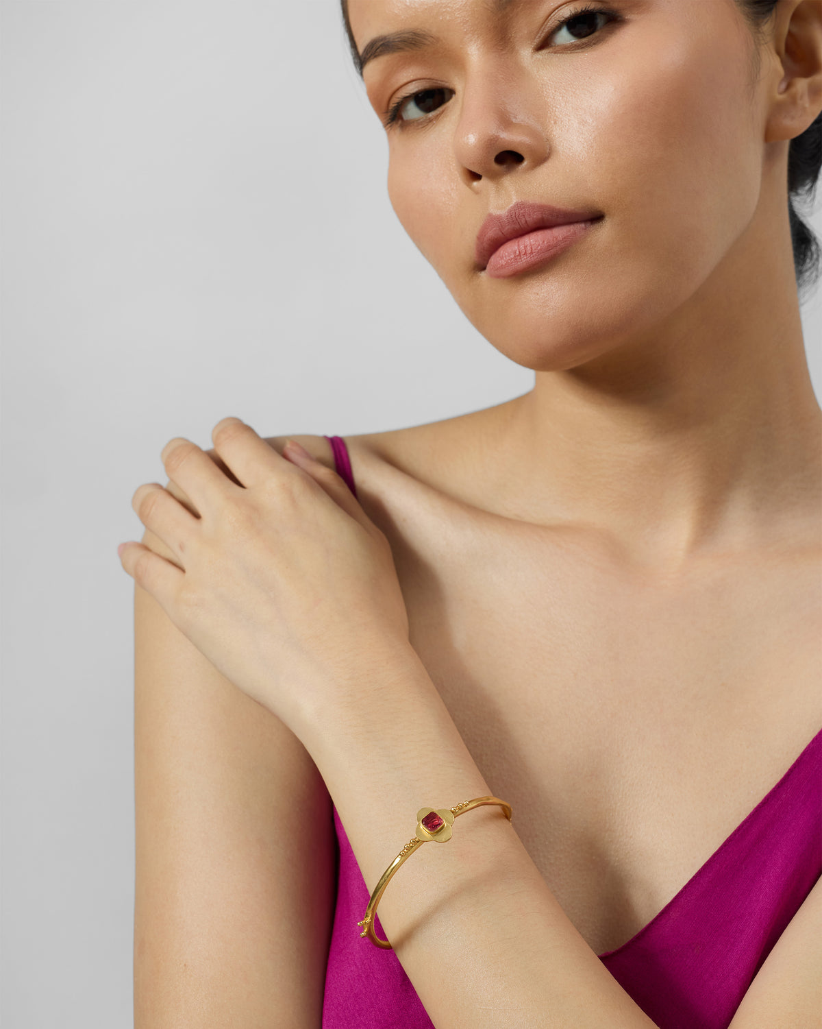 Person wearing a gold Ahiliya bangle with a pink glass motif.