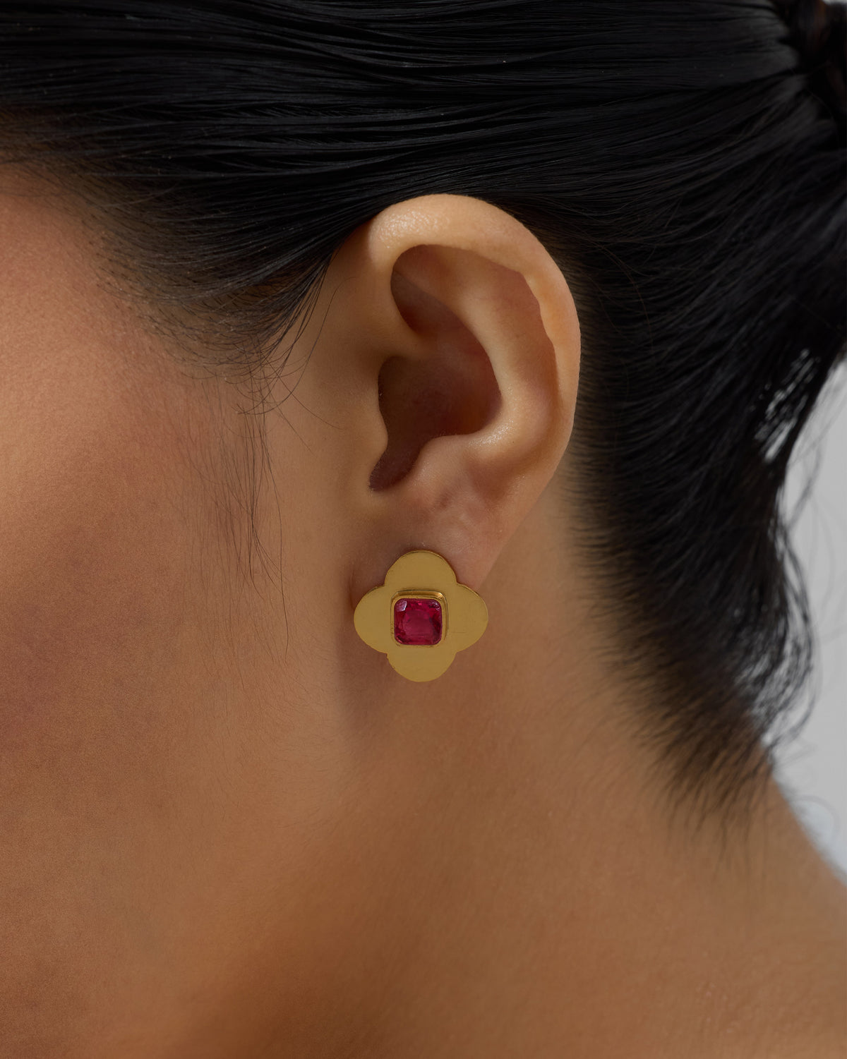 Side profile of a gold Ahiliya stud with pink glass on a person.