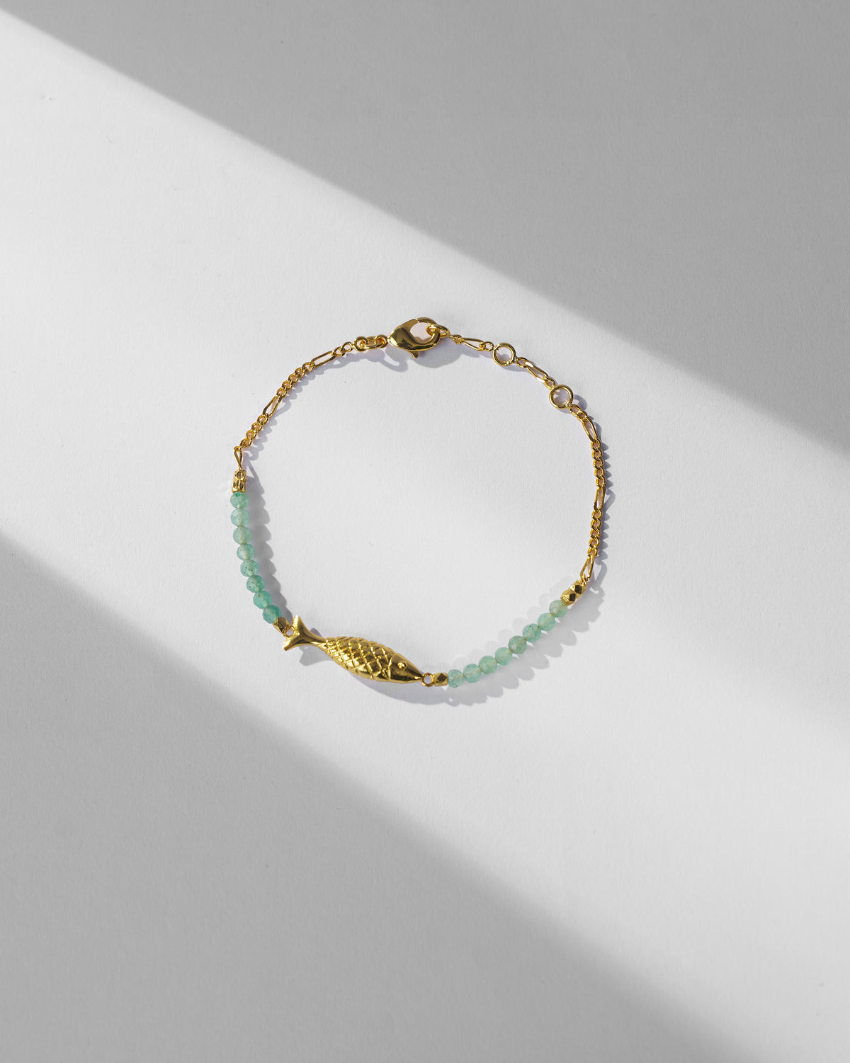 Gold Maase bracelet with green beads, fish charm, chain and lobster clasp.