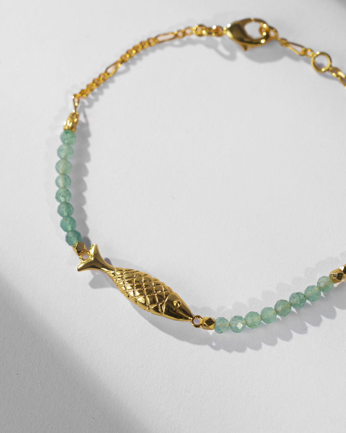 Close-up of the gold Maase fish charm with pale green faceted beads.