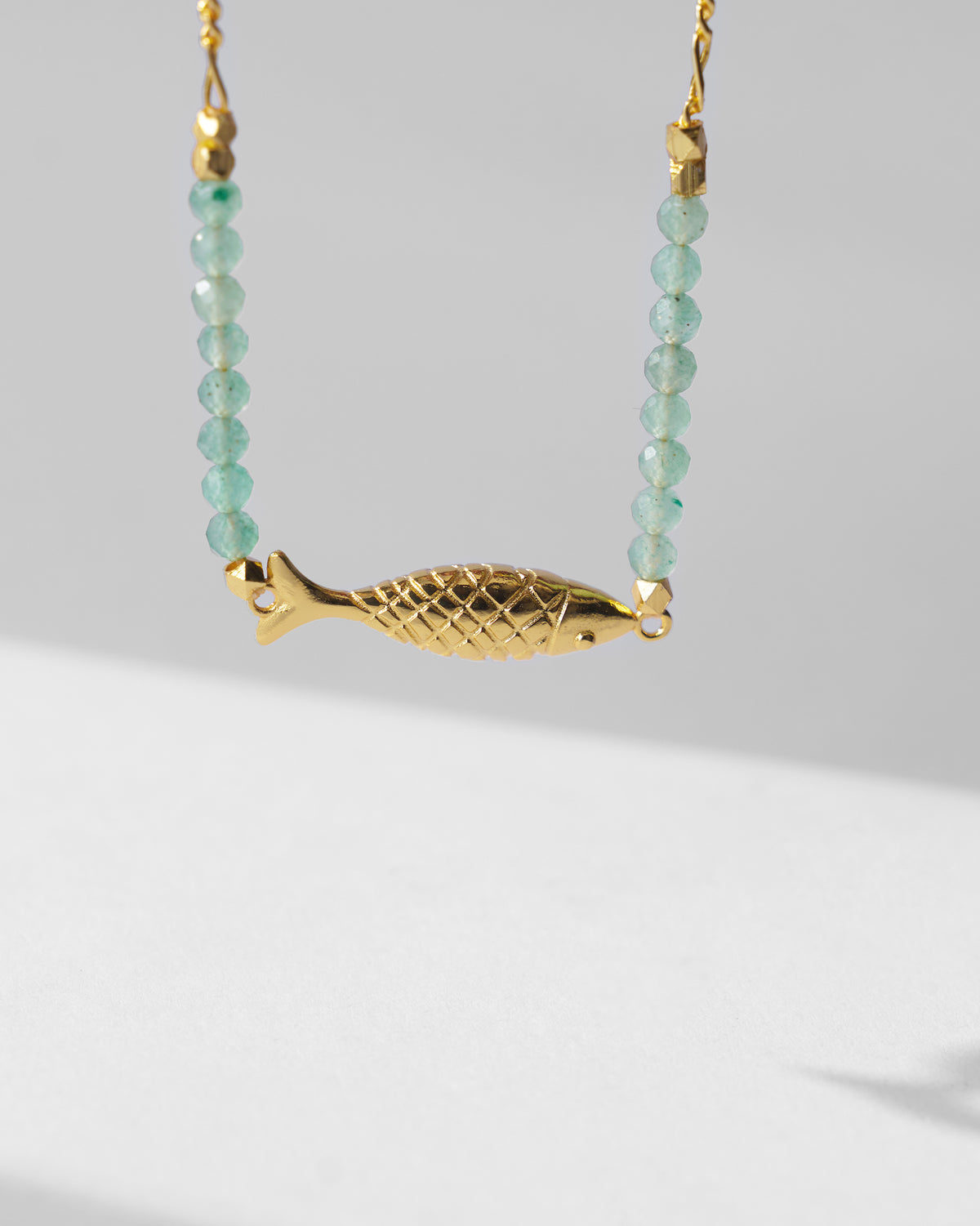Gold Maase bracelet showing the fish charm between green bead strands.