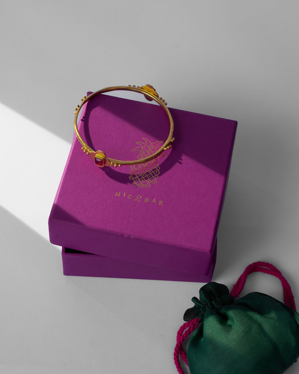 Gold Double Loop Bangle on a magenta Nicobar box with a green pouch.
