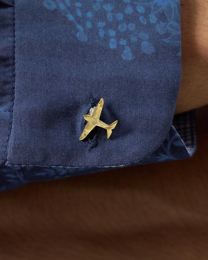 Close-up of a gold airplane cufflink on a navy shirt cuff.