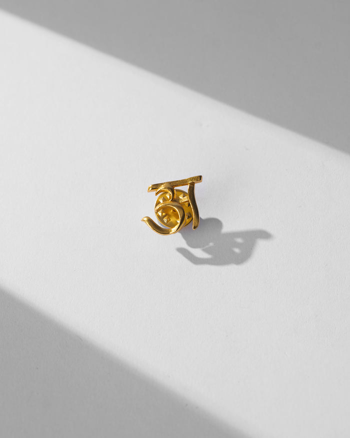 Close-up of gold Alphabet A Pin on a white surface.