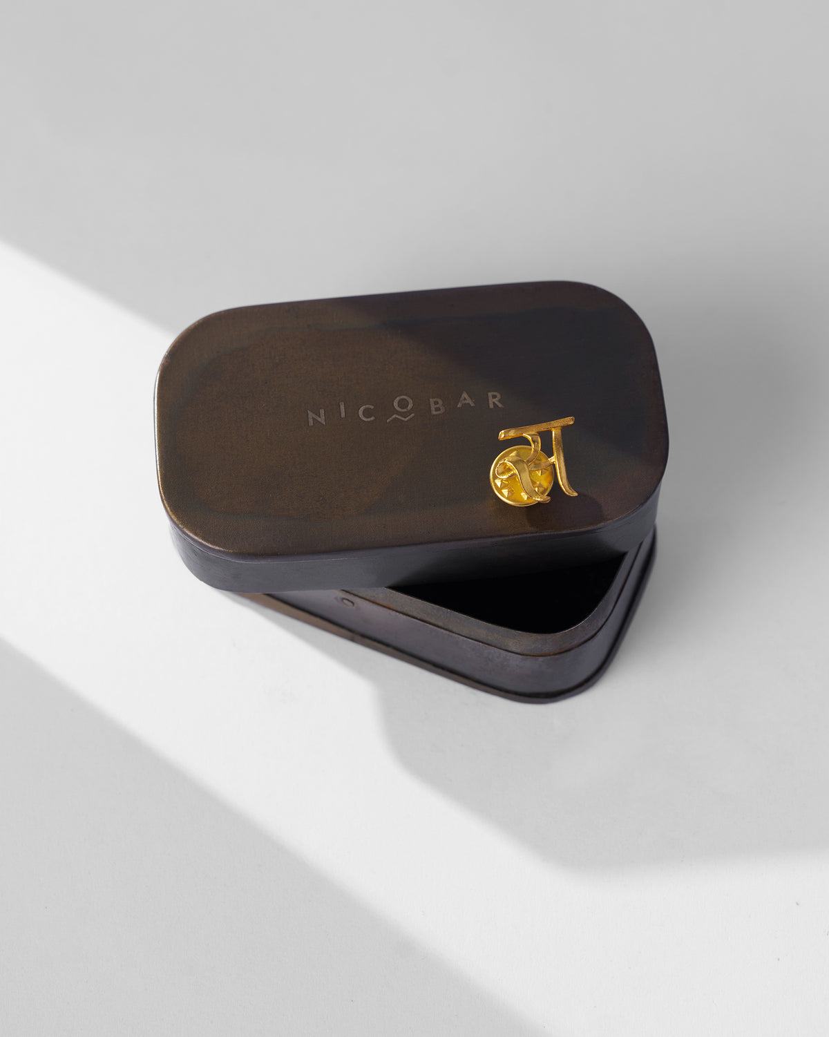 Gold Alphabet S Pin on the lid of a Nicobar tin.