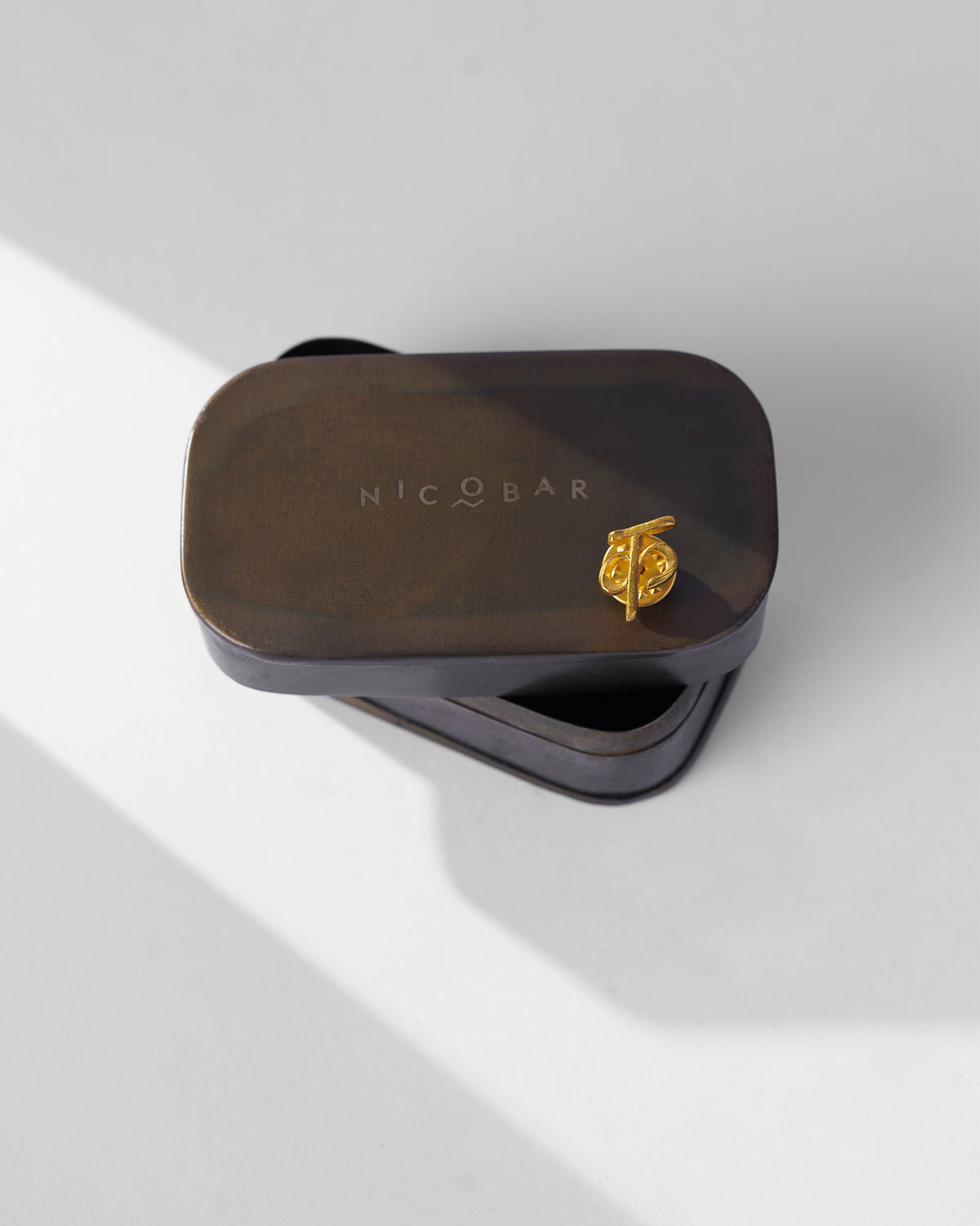 Gold Alphabet K Pin on the lid of a Nicobar tin.