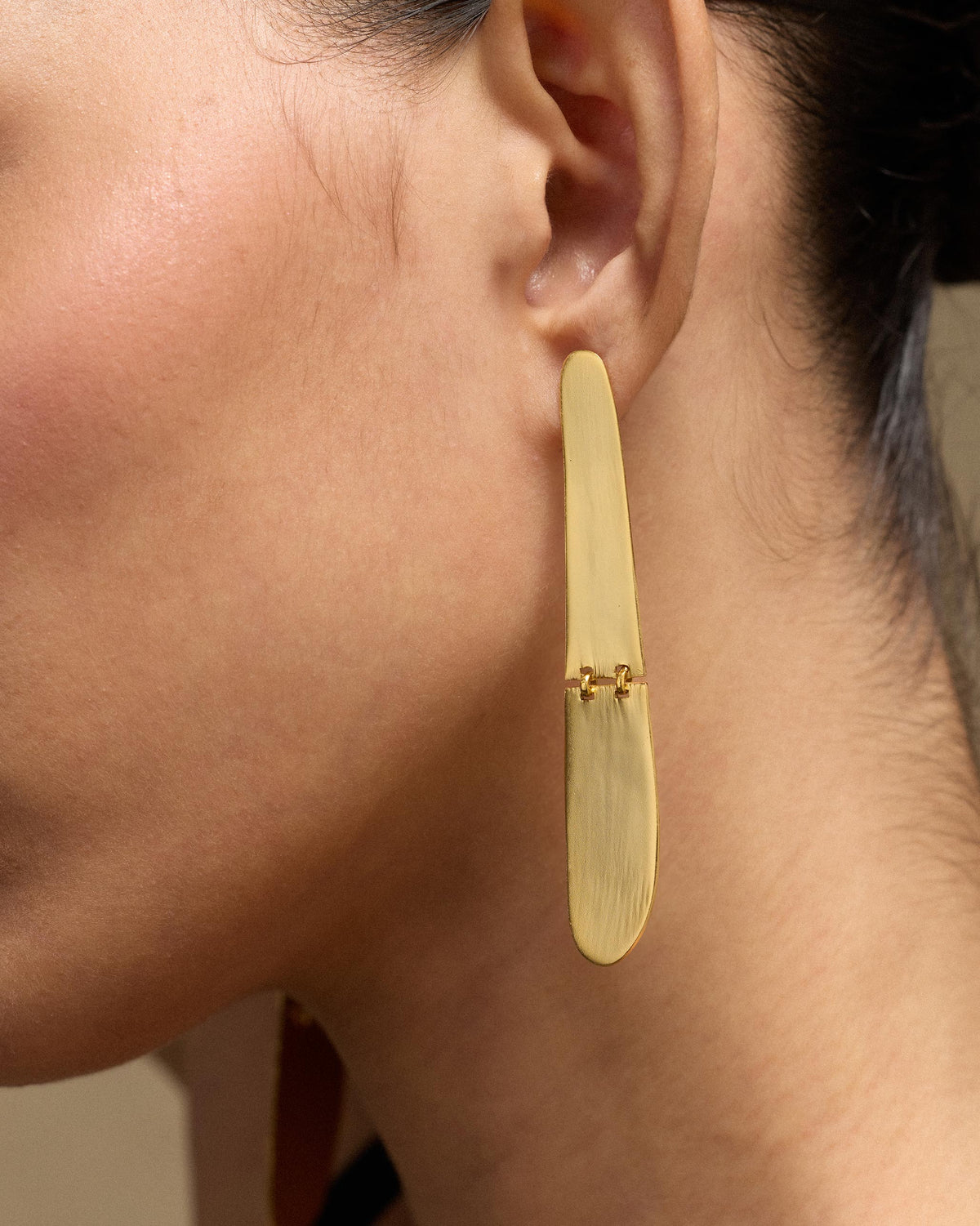 Close-up of a long gold Yamuna Earring worn on an ear, showing its small link detail.