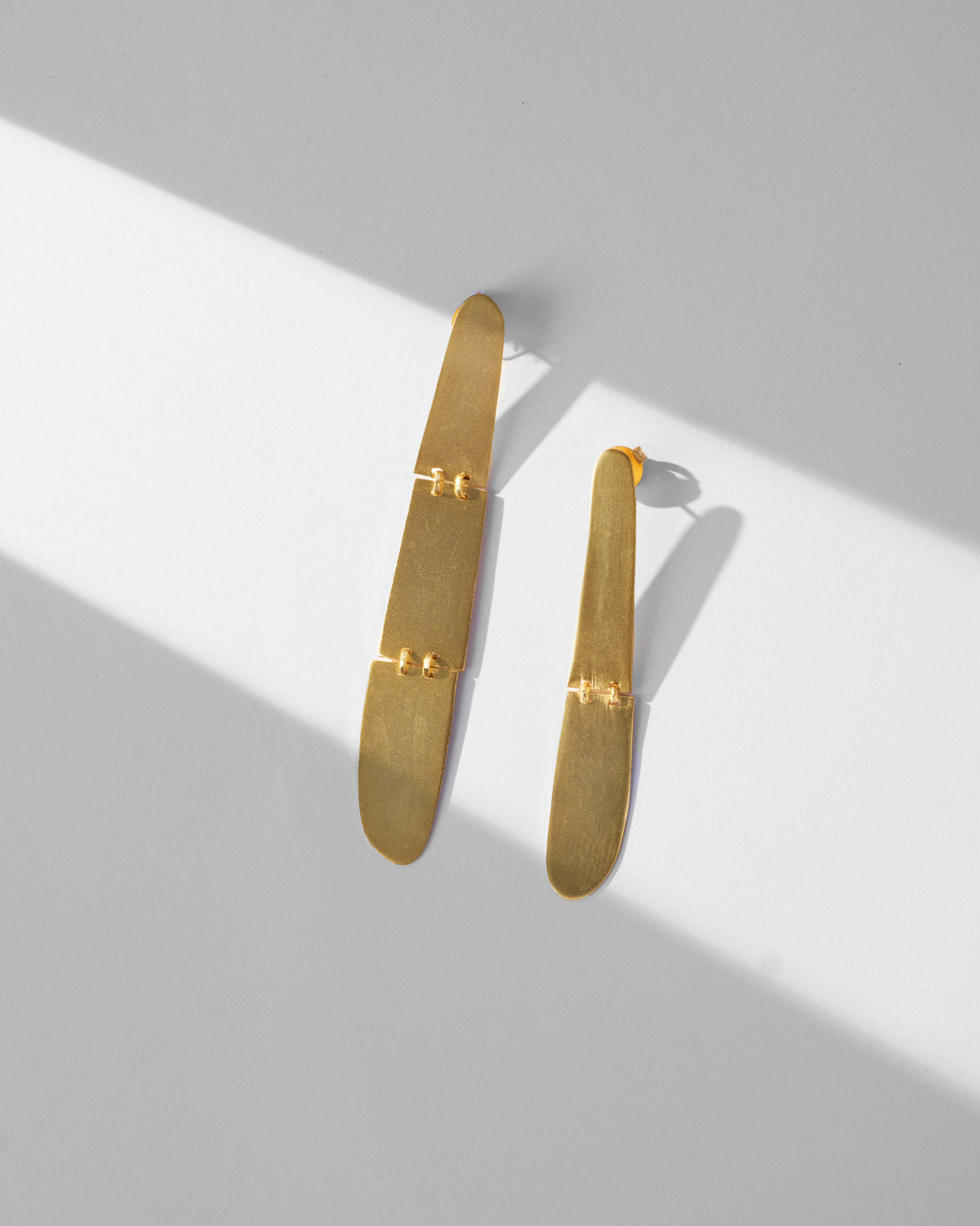 Pair of long gold Yamuna Earrings laid flat, with small link details.
