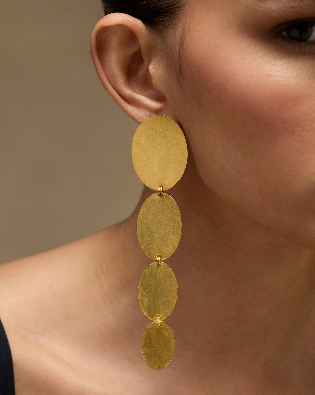 Close-up of a gold Drift Danglers earring with four oval discs hanging from the ear.