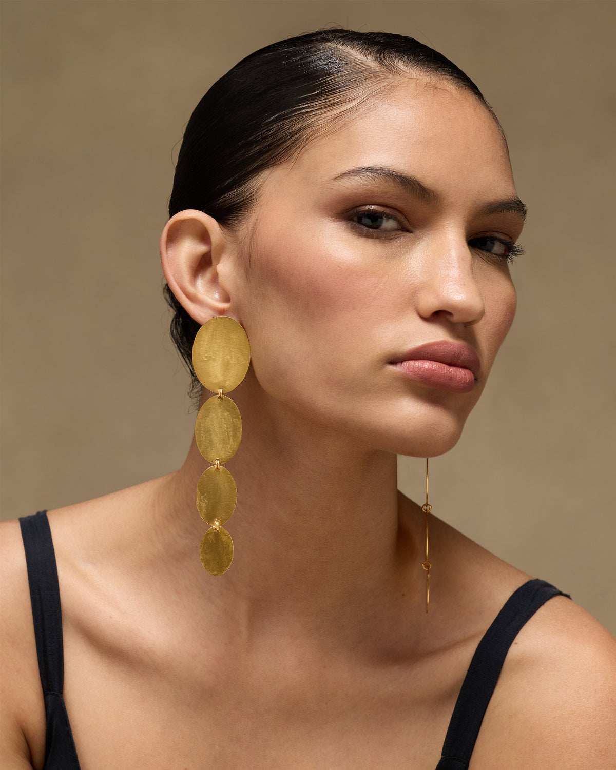 Person wearing a long gold Drift Danglers earring with four discs.