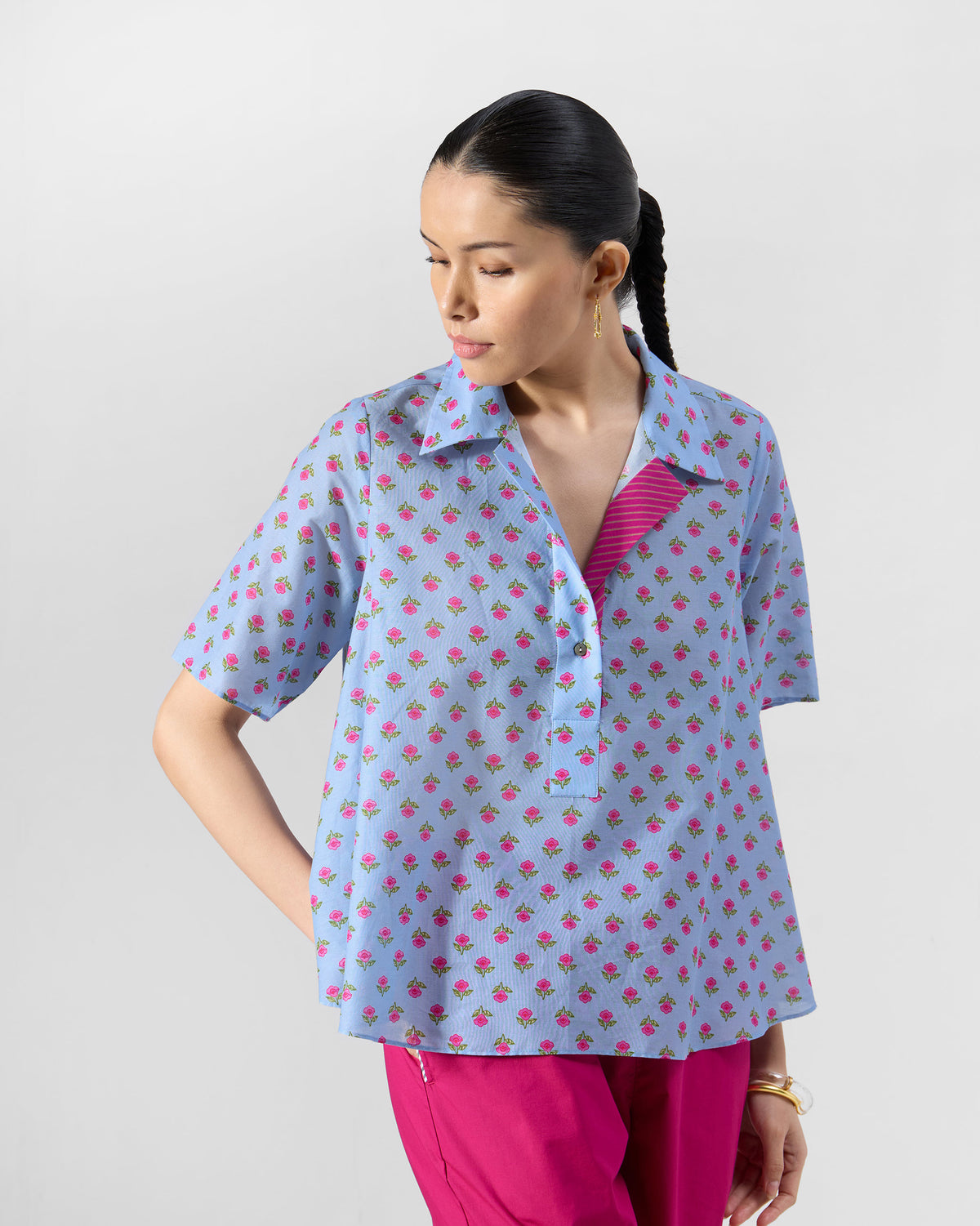 Person wearing an ice blue Rann shirt with a pink rose print and contrast placket lining.