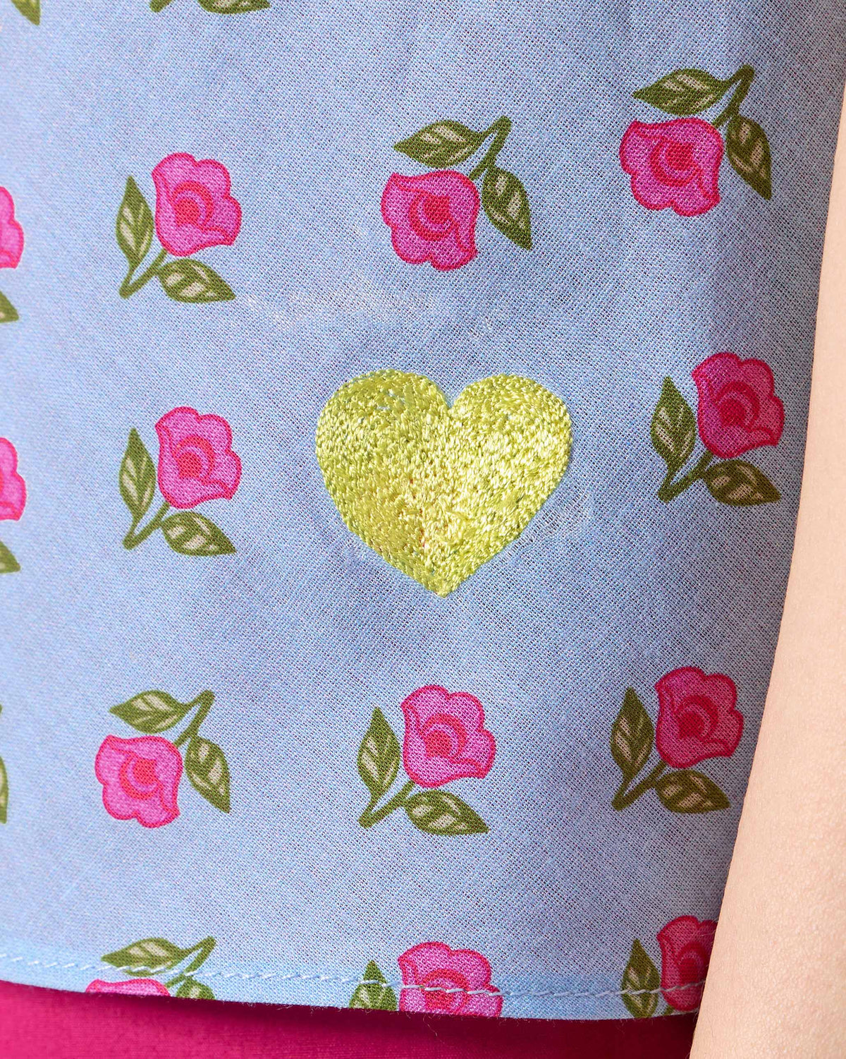 Close-up of a lime green embroidered heart on an ice blue Rann shirt.
