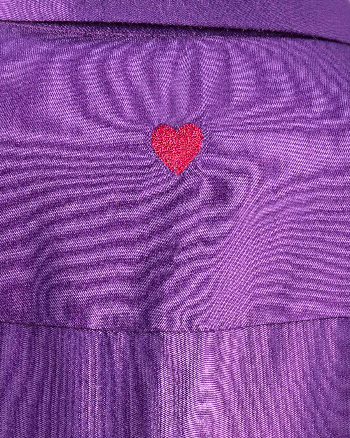 Close-up of a red embroidered heart on a purple Katya shirt.