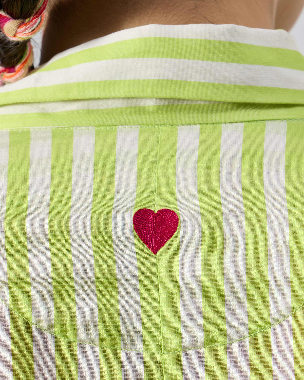 Close-up of a pink embroidered heart on a lime striped Manoor Top.