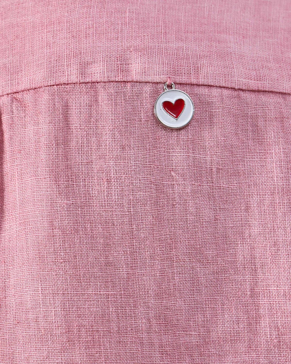 Close-up of a red-heart charm on soft pink Mati linen.