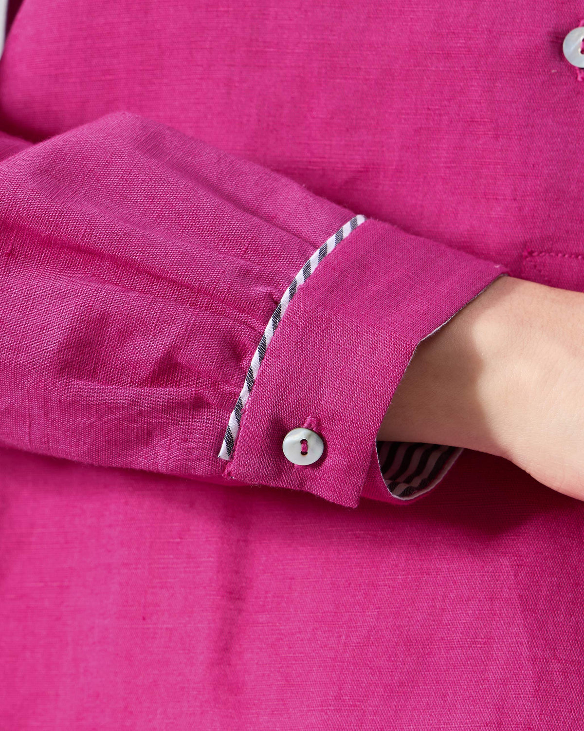Close-up of a berry pink Mati shirt cuff with black and white striped trim.