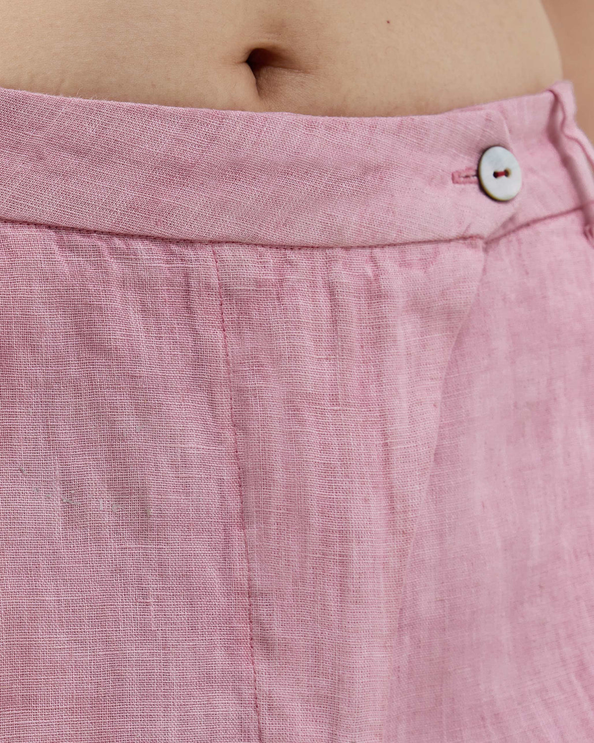 Close-up of the pearl button and linen weave on soft pink Aven pants.