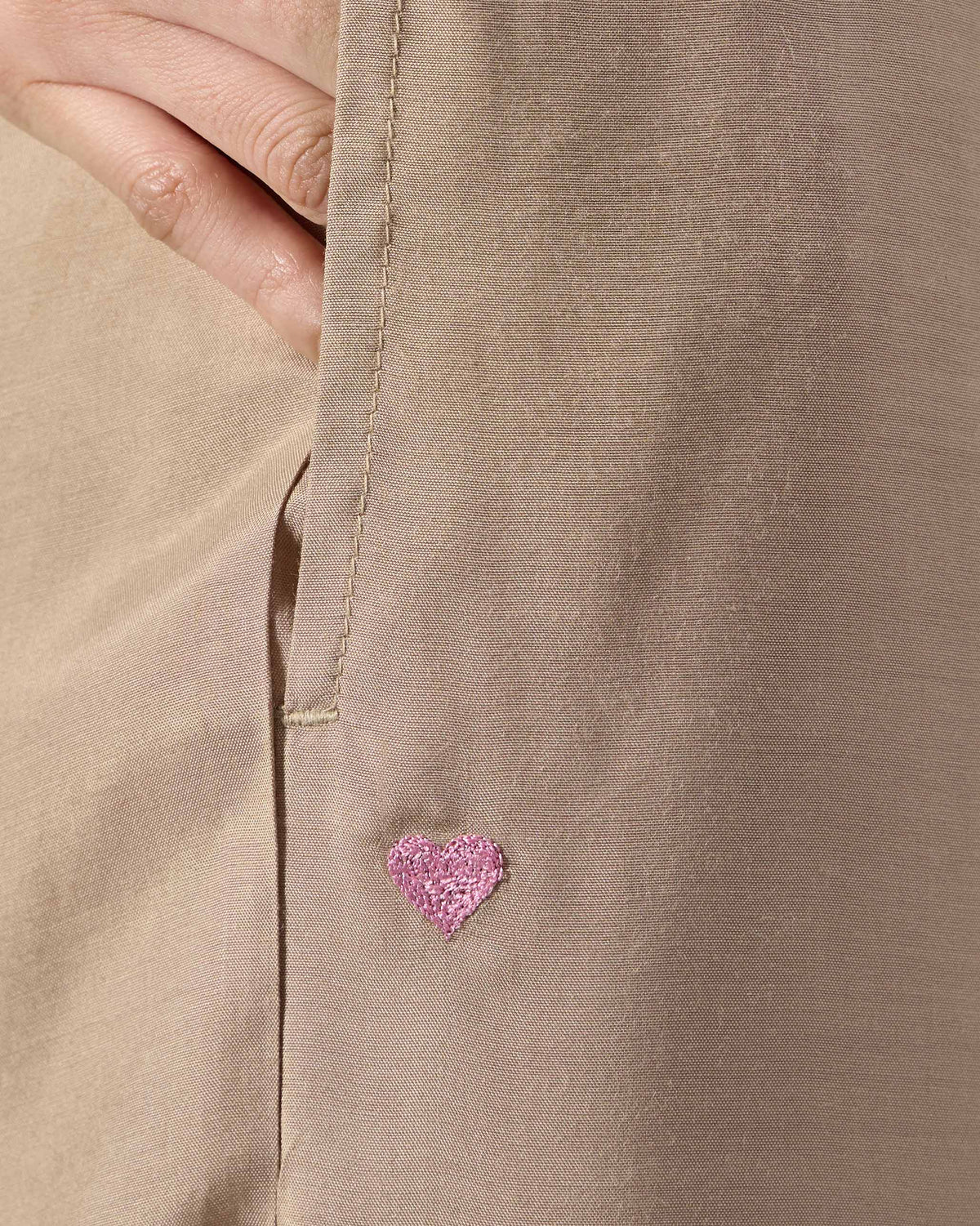 Close-up of sand Bemberg narrow pants pocket with a pink embroidered heart.