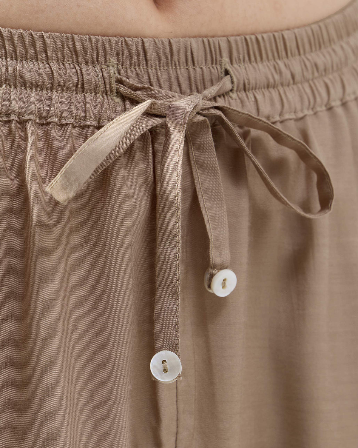 Close-up of a sand Bemberg narrow pants drawstring waist with white button ends.