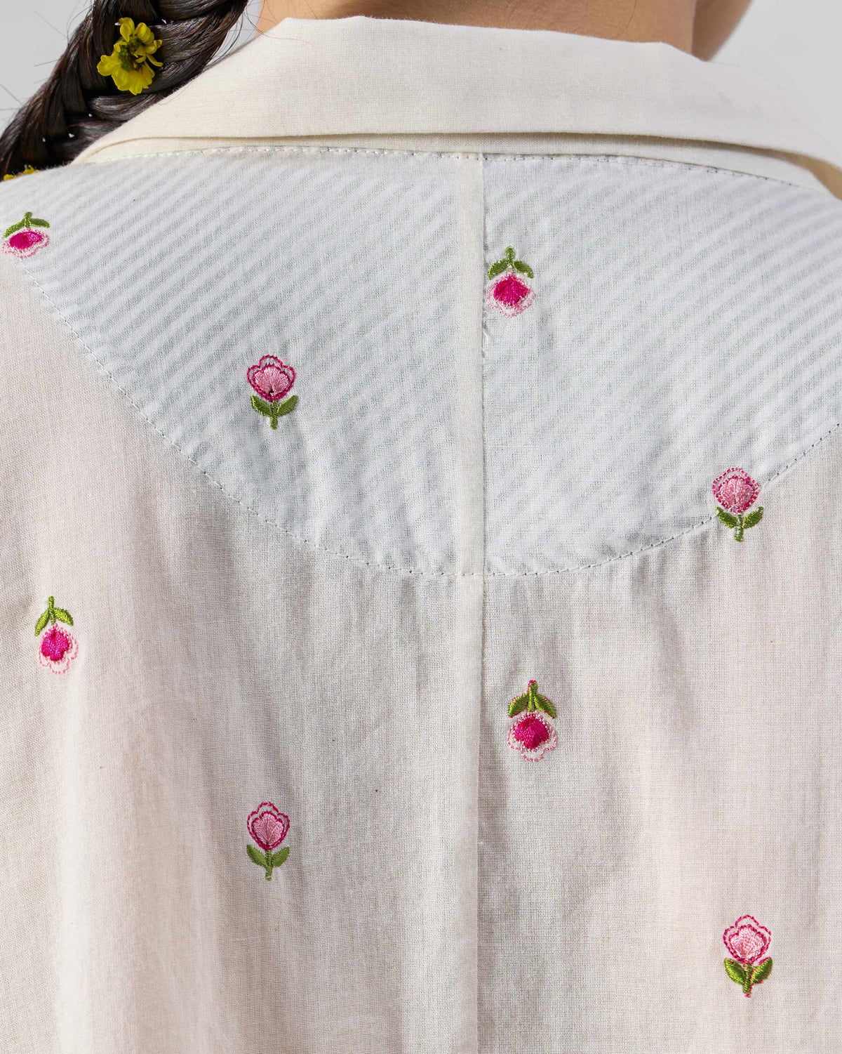 Close-up of a pinstripe back yoke with pink floral embroidery on an ivory shirt.