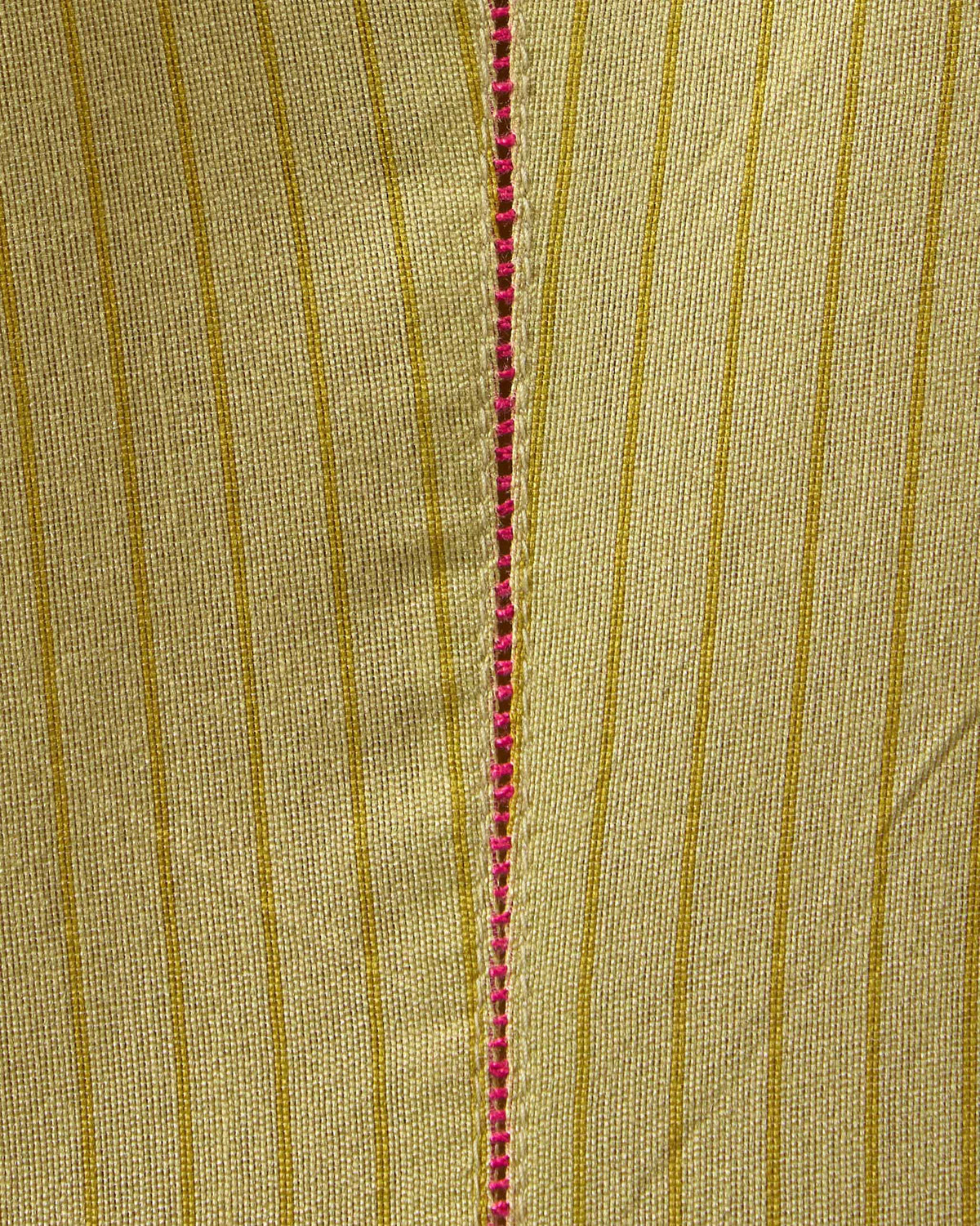 Close-up of sand Murud kurta fabric with pink ladder stitching along a seam.