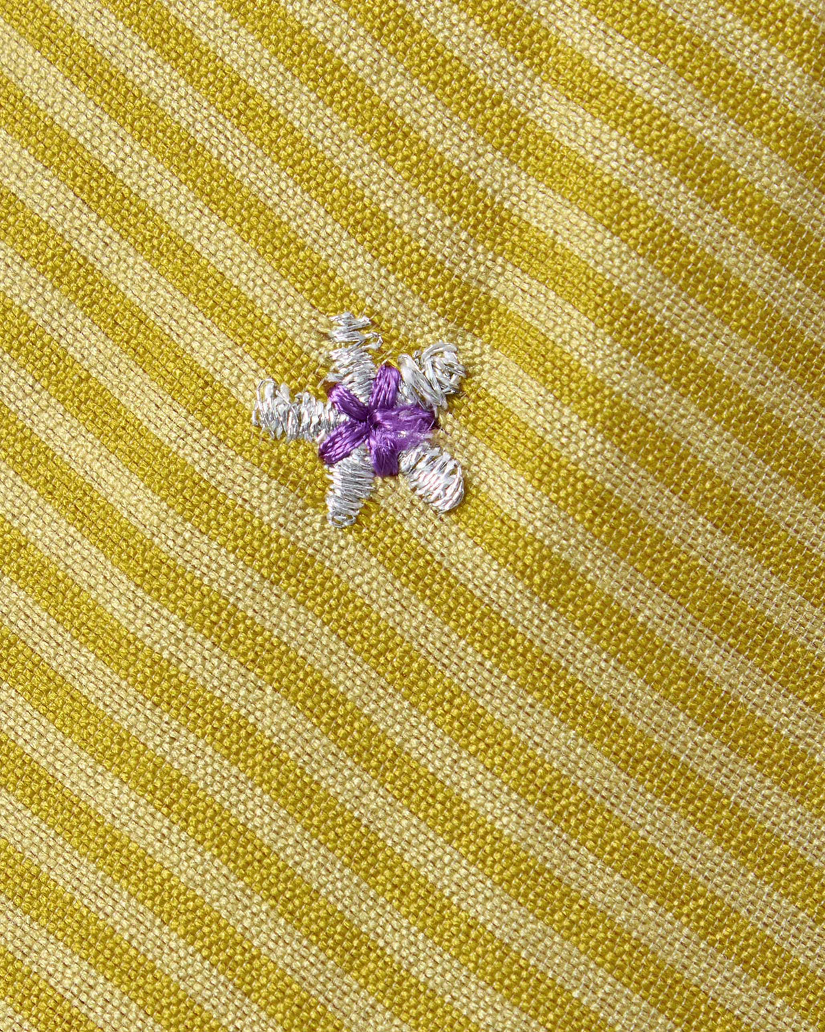 Close-up of sand Murud kurta fabric with a purple and silver embroidered motif.