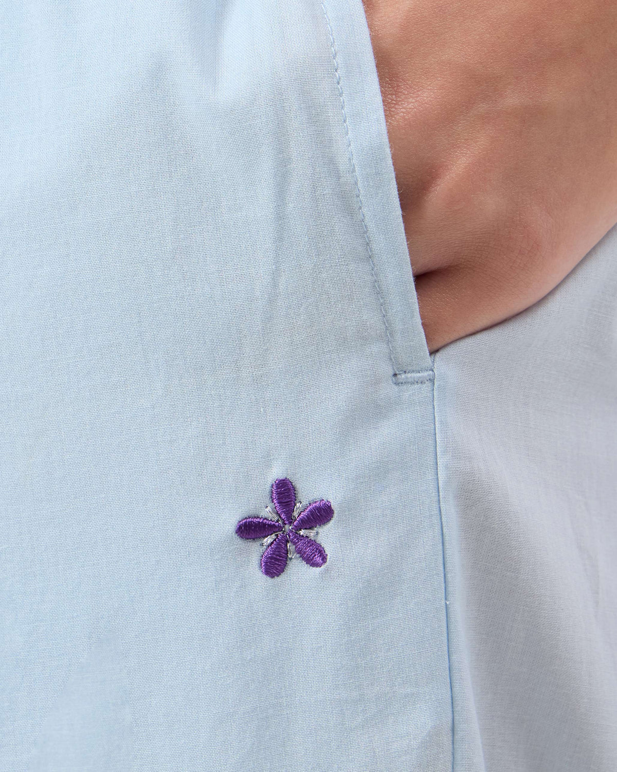 Close-up of a purple flower embroidered near the pocket of ice blue Narrow Pants.