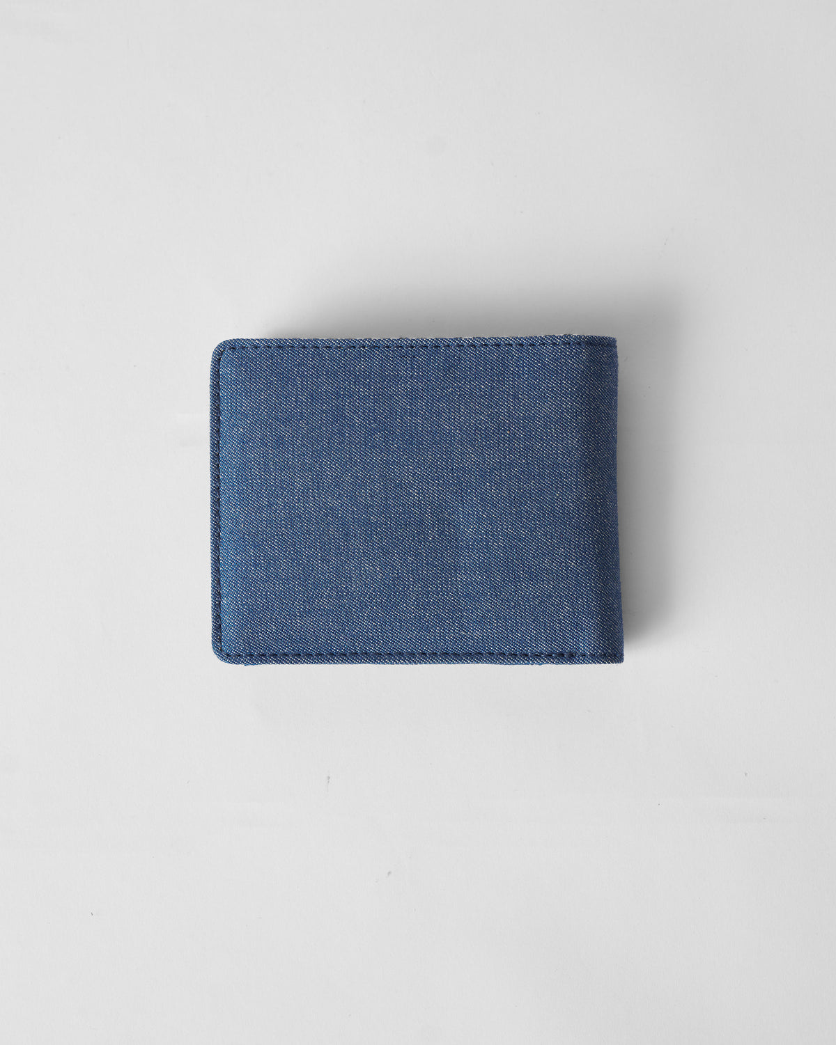 Back of a denim blue Classic Bi-Fold Wallet laid flat.